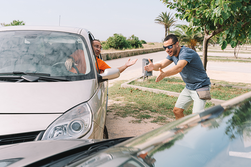 Unsafe driving. Accident between two cars with 2 people outdoors