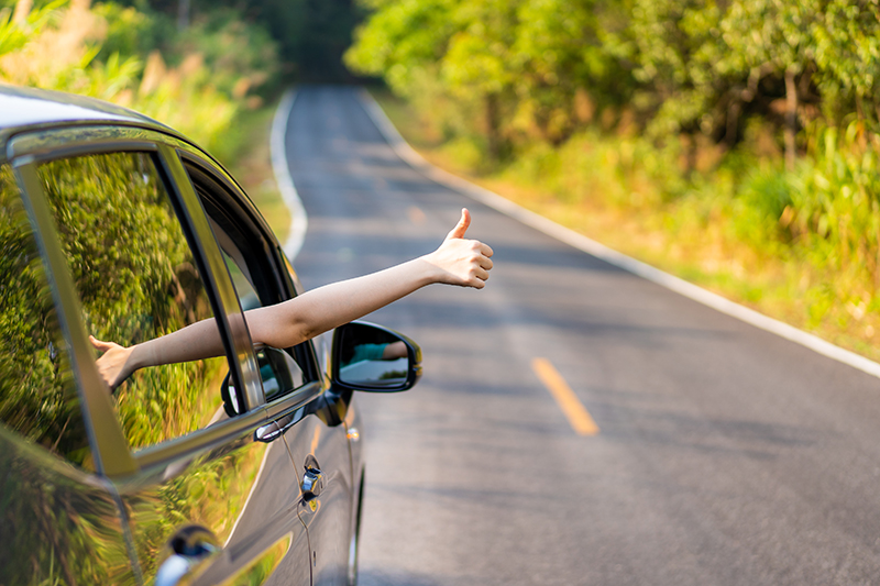 Woman in the car showing her thumb up sign.  Safe driving is relaxed driving.